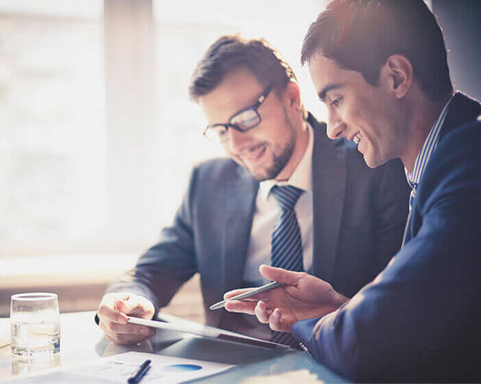 Two businessmen in suits holding pens looking at a document.