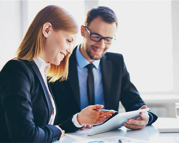 A businessman and businesswoman in professional clothing sitting down and looking at a document together.