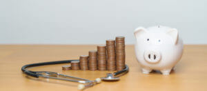 An image featuring a stack of coins, a piggy bank, and a stethoscope to illustrate a cancer compensation claim.
