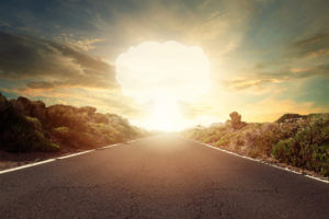 A nuclear bomb explosion with a mushroom cloud on the horizon and an empty desert road from a nuclear test.